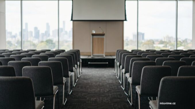 Prázdný konferenční sál s řadami židlí a řečnickým pultem